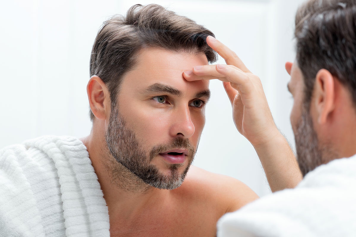 Brunette guy looking at his forehead wrinkles in the mirror