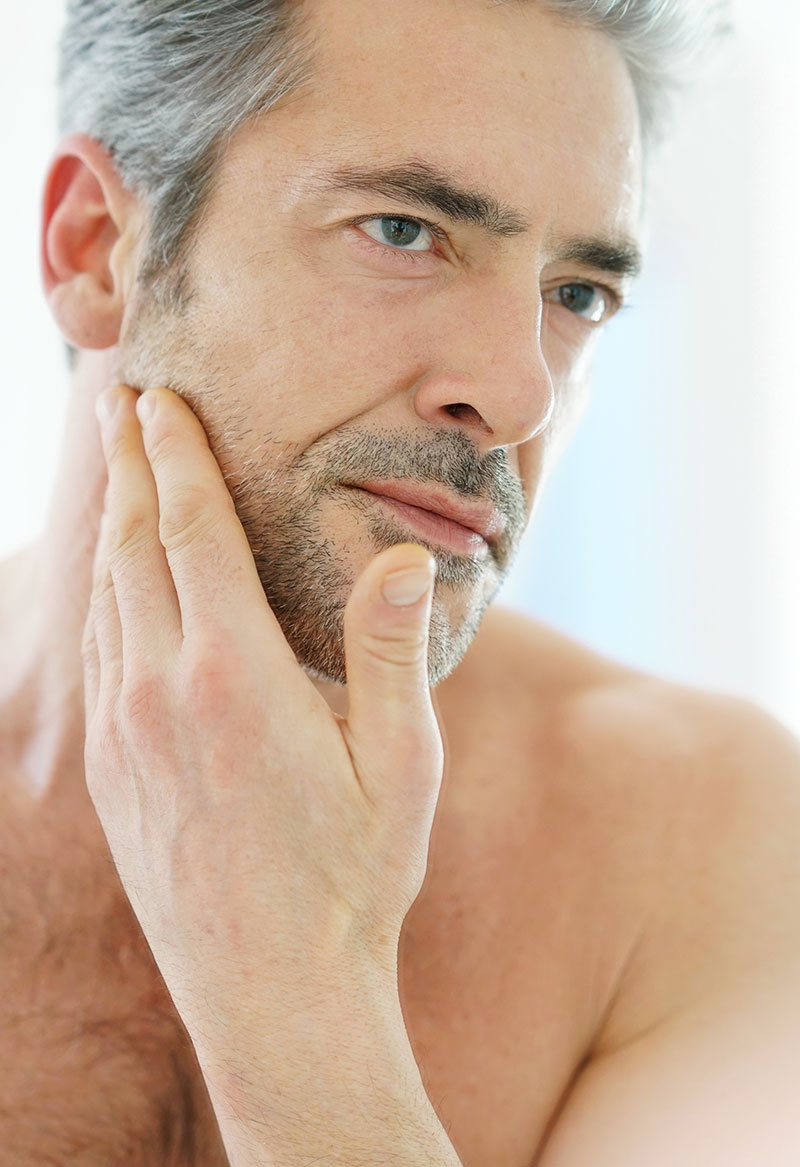 Older man touching his stubble in the mirror