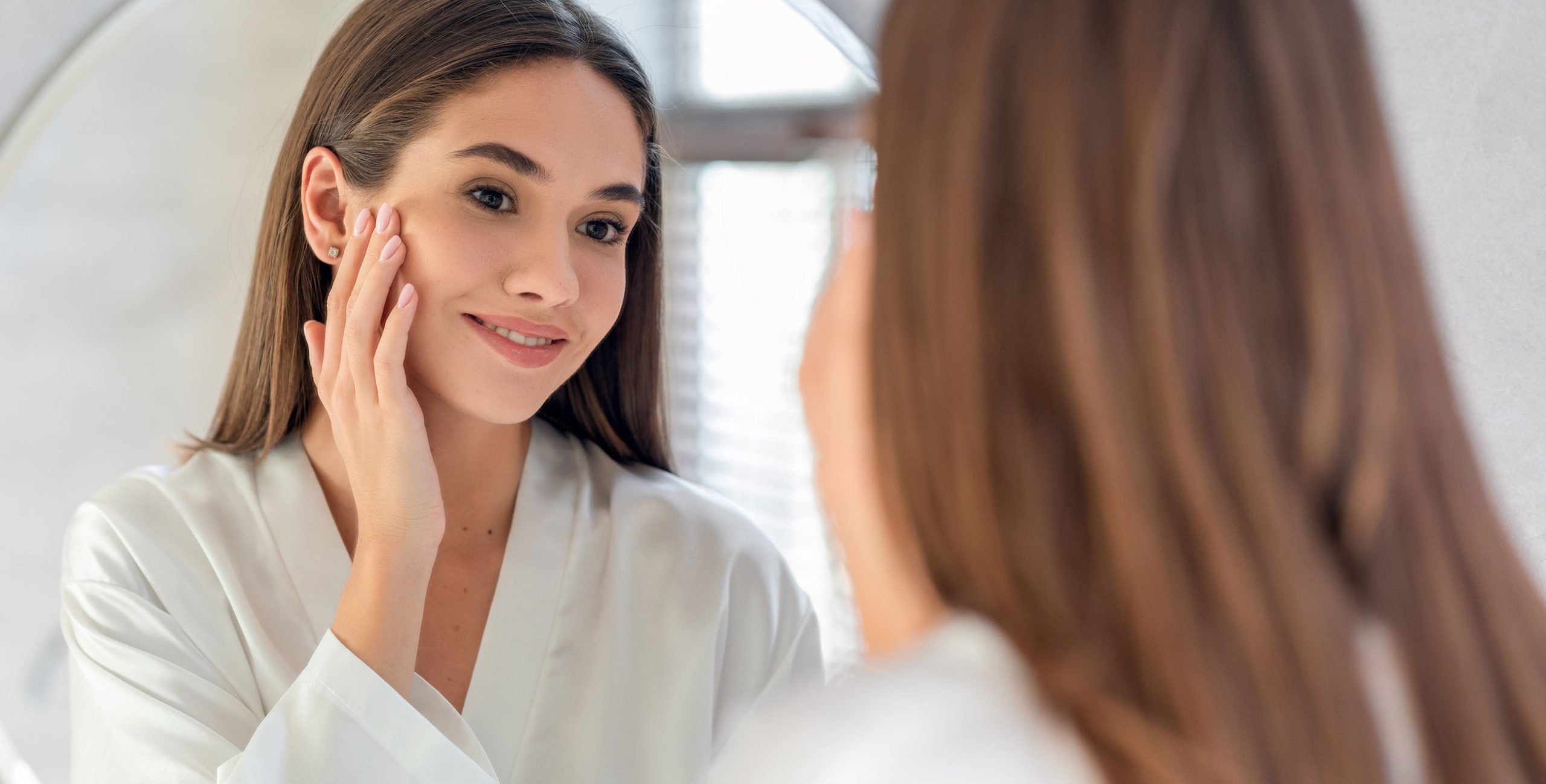 Young brunette lady looking at her flawless skin in the mirror