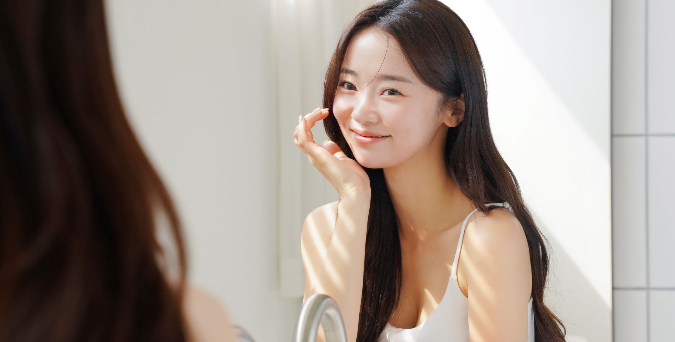 Asian lady smiling in the mirror admiring her flawless face