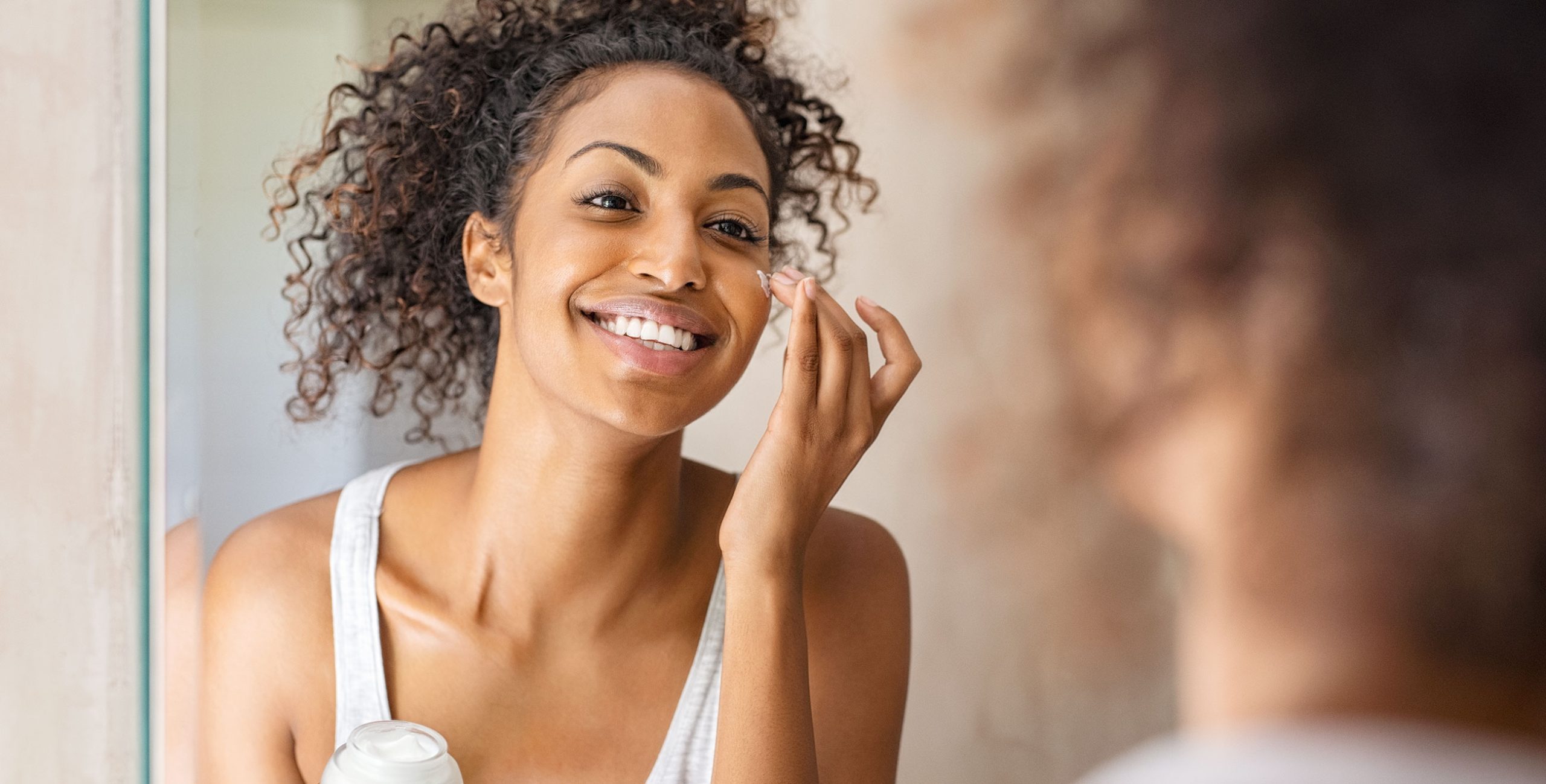 Lady applying moisturizer on her face in the mirror