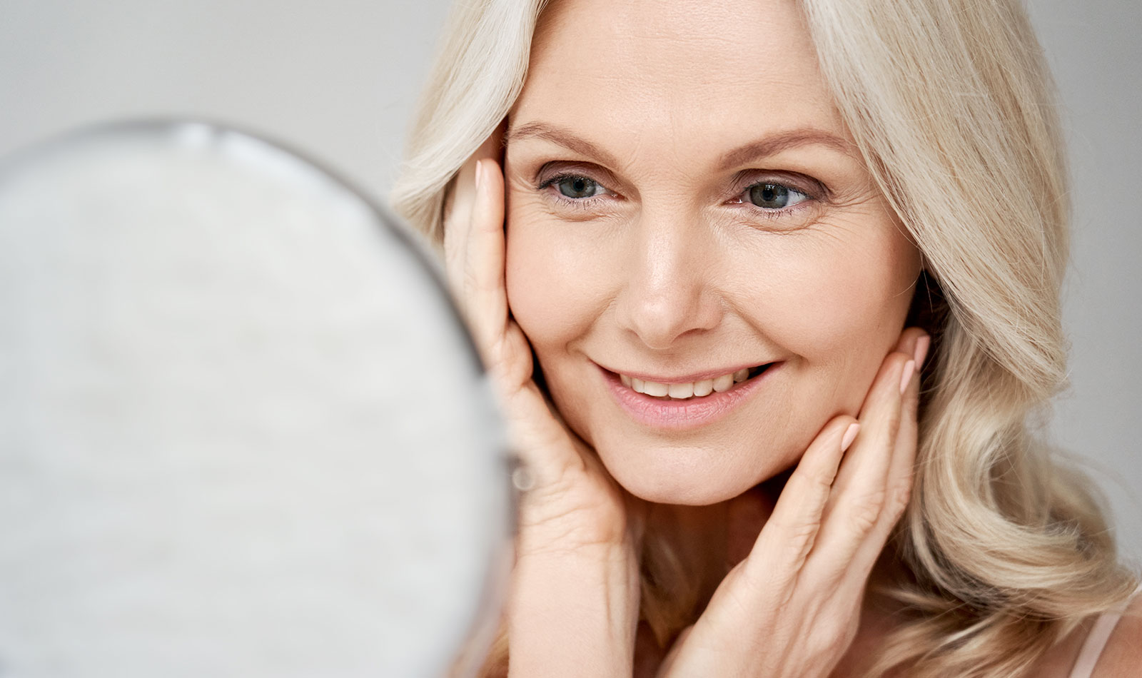 Blonde lady looking at her flawless face in the mirror